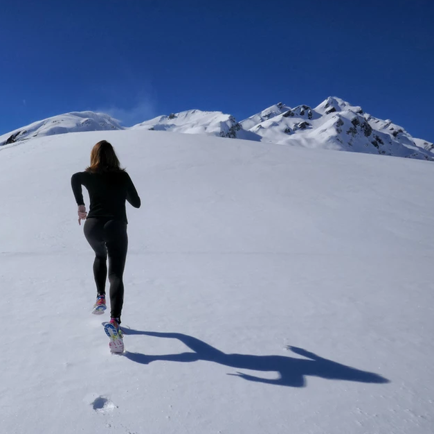 Woman running up snowy mountain.